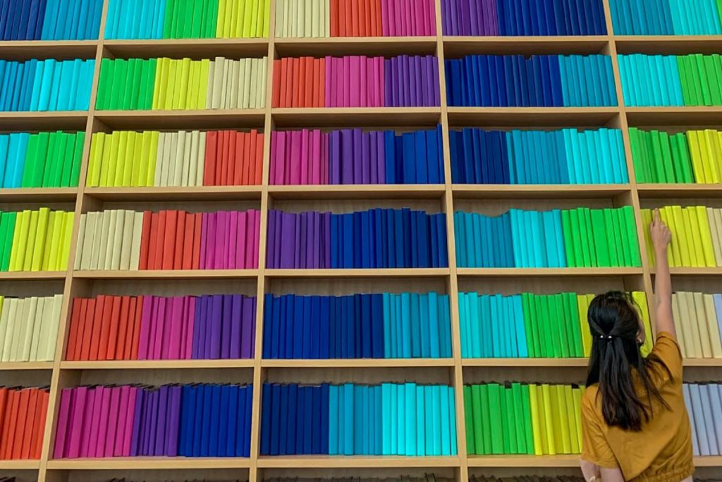 Rainbow of books spread across multiple library shelves