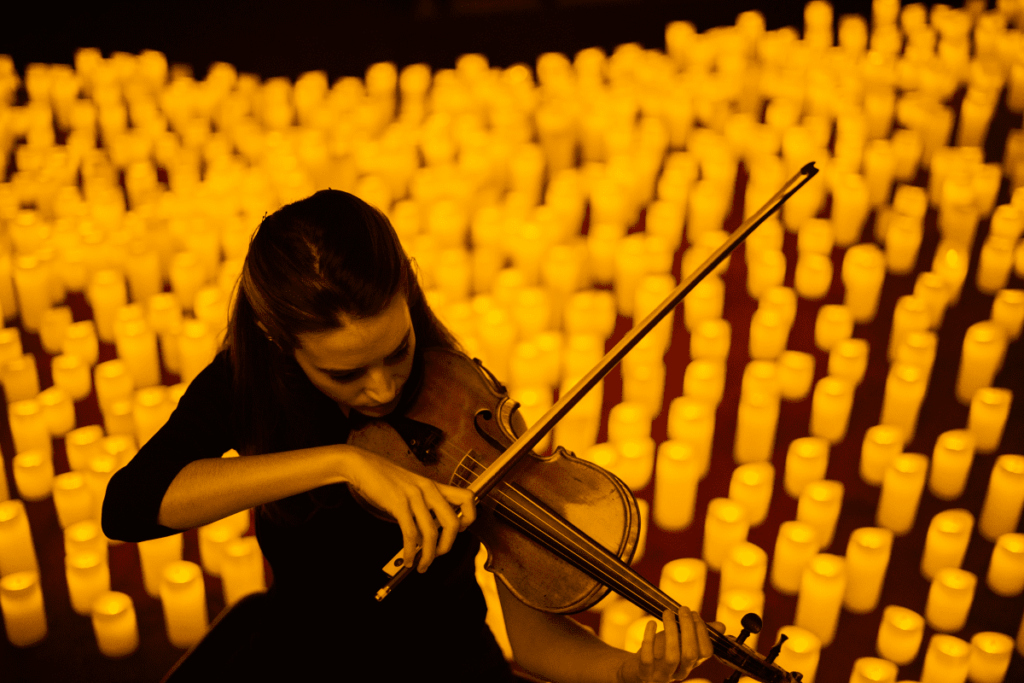 An angle-shot of a violinist playing on a stage surrounded by hundreds of candles