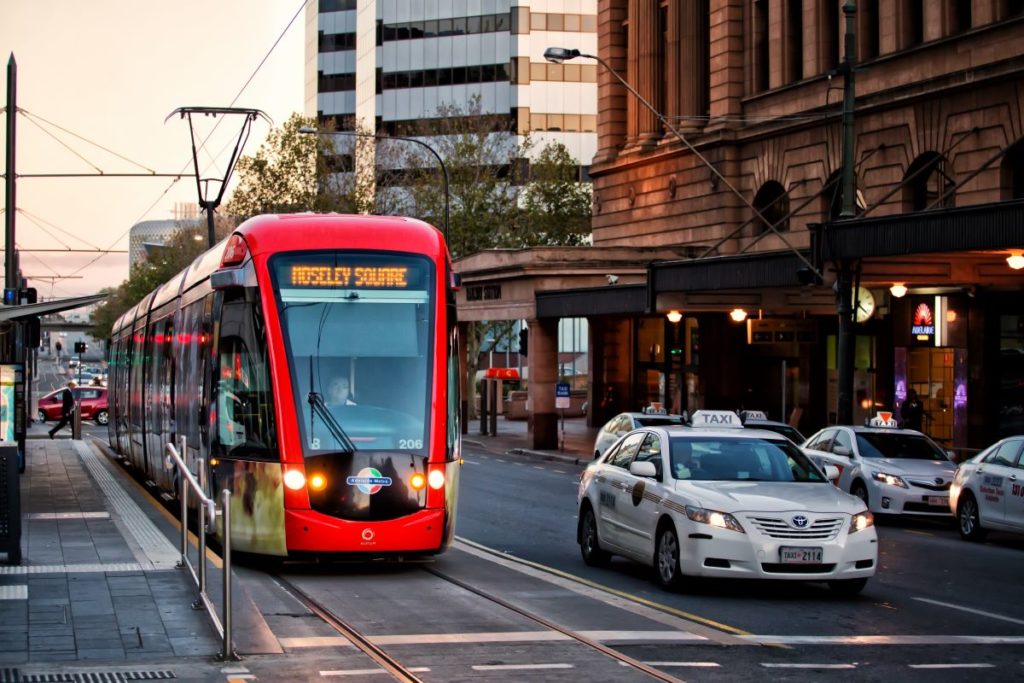 Main road in Adelaide's city centre with a red tram and taxi next to each other on the road