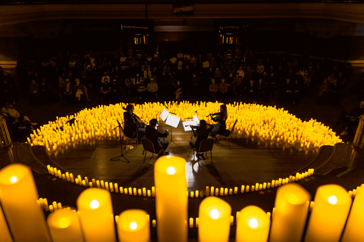 A string quartet seen, behind a close up of seven candles, performing surrounded by candles.