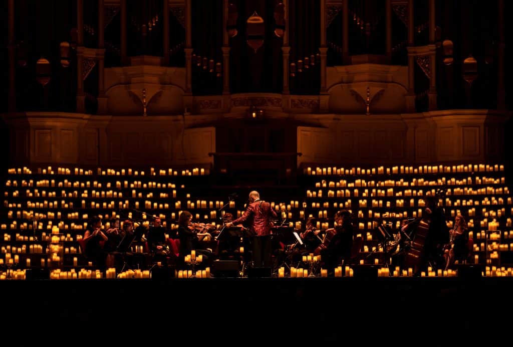 conductor and orchestra on stage surrounded by hundreds of candles