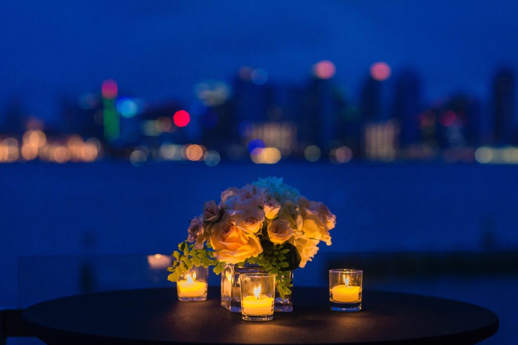 A romantic restaurant overlooking water with flowers and candles on a table.