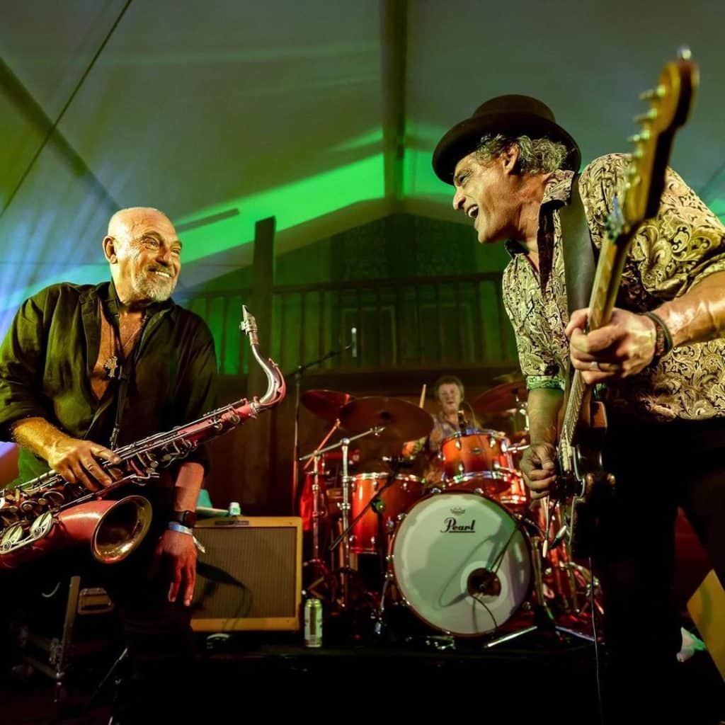 Joe Camillerio of The Black Sorrows on stage with a saxaphone and a guitar player
