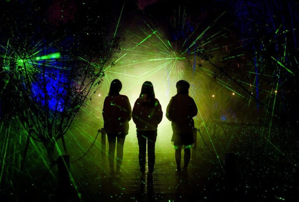 Three people walking into the darkness surrounded by green lasers