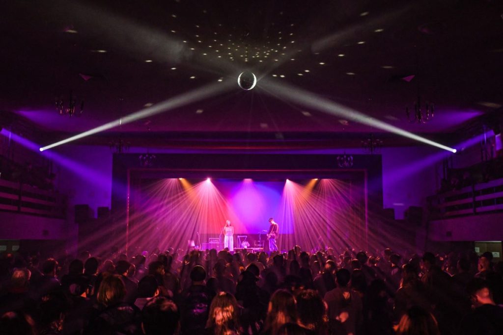 Concert hall illuminated with hues of purple/disco ball