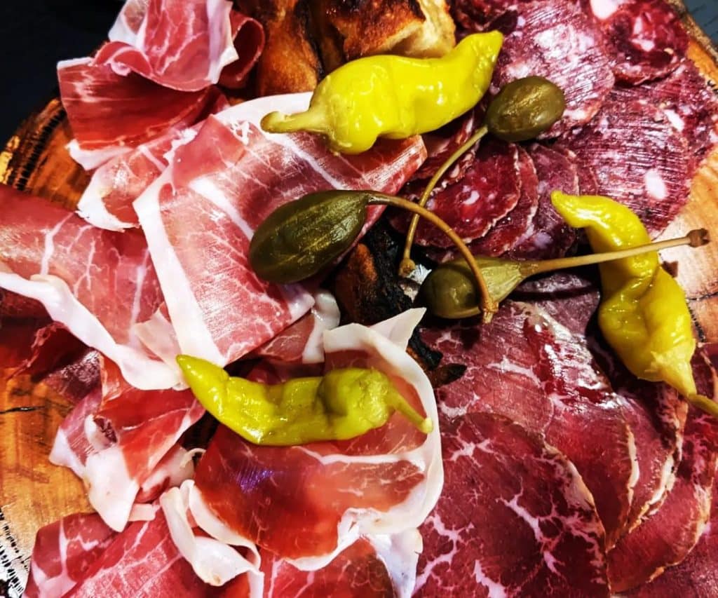 Charcutterie board of sliced meat, capers, and peppers