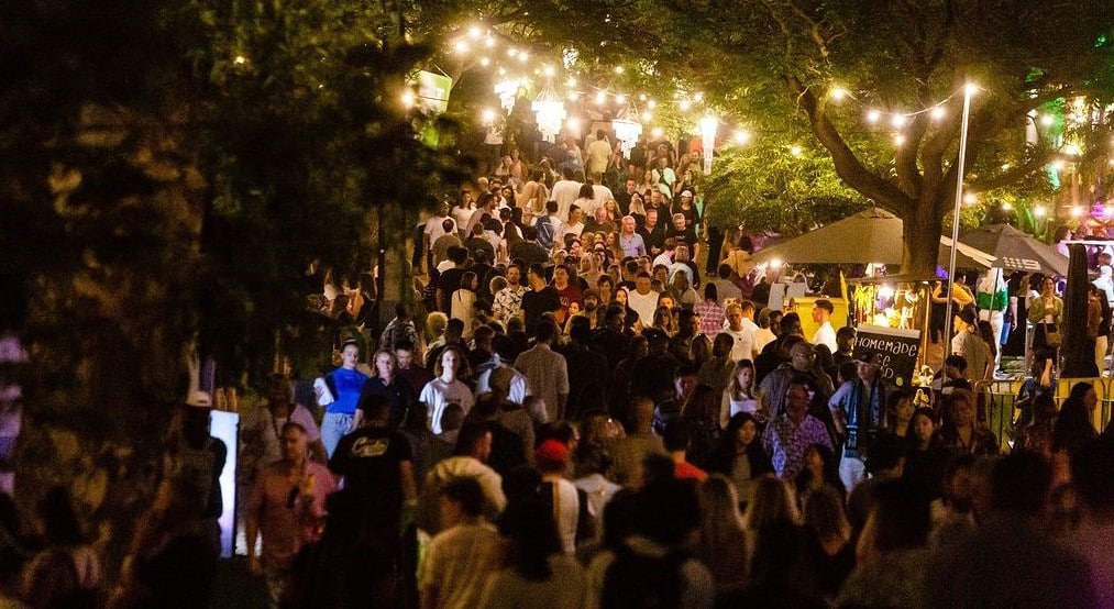 Crowds of people walking through path amongst trees with overhanging lights at nighttime