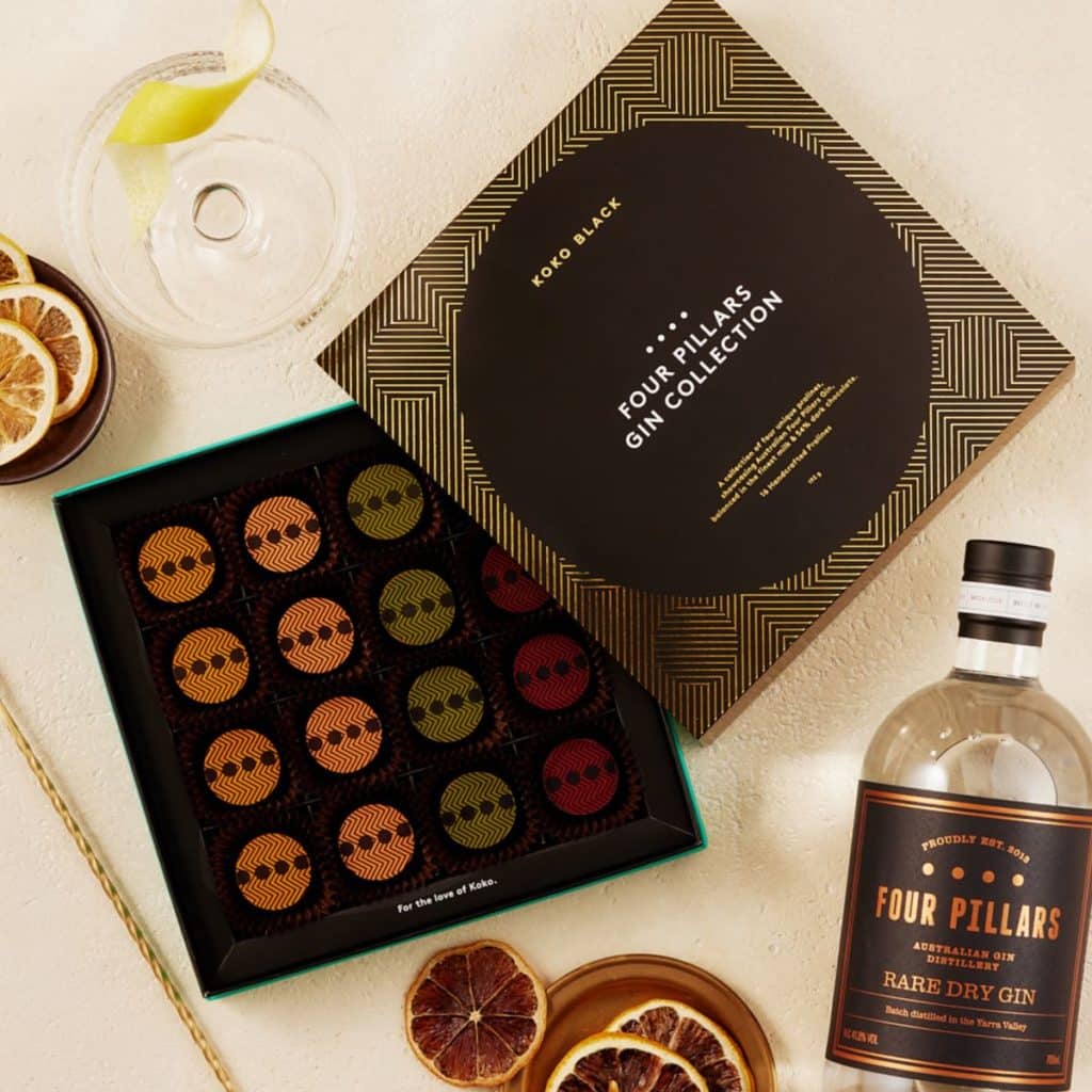 Flatlay of an open box of colourful chocolates, bottle of gin, fried fruits,