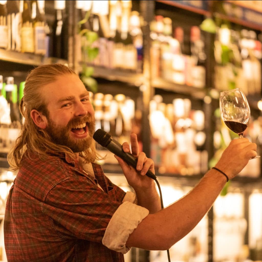 Bartender with a microphone holding up a wine glass and laughing