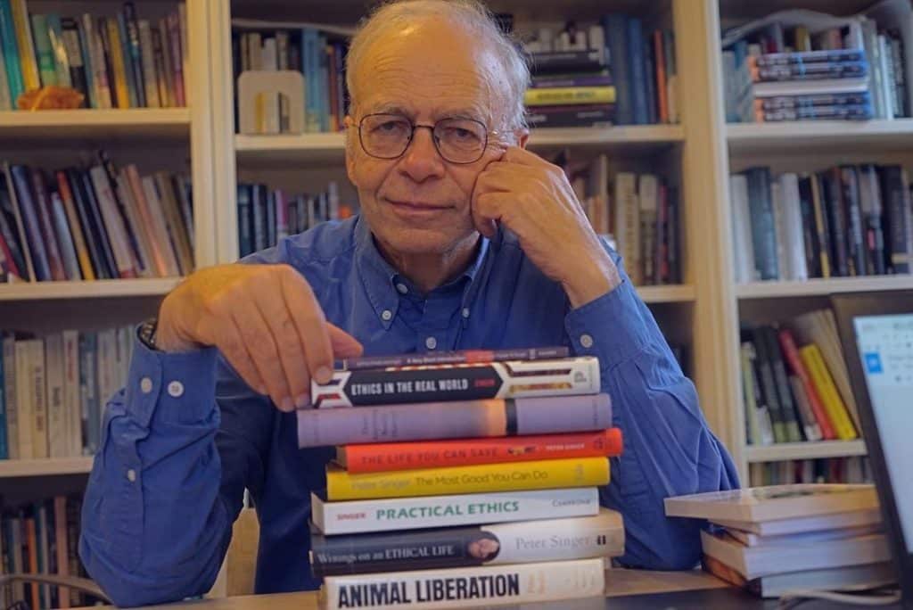 Peter Singer sitting behind a stack of books in a library
