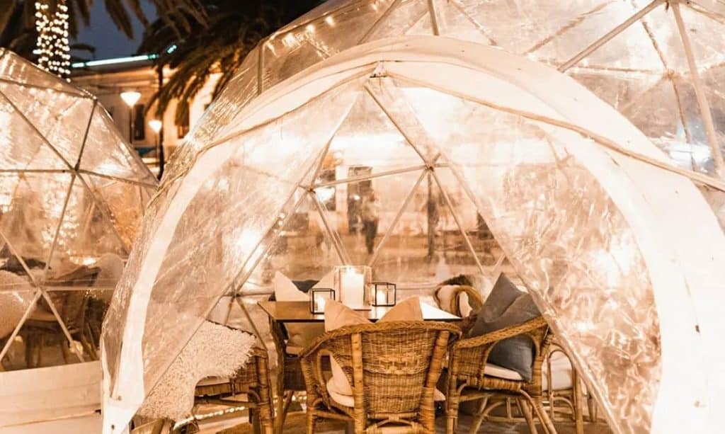 See-through igloo with dining table and chairs inside with polliws and blnkets